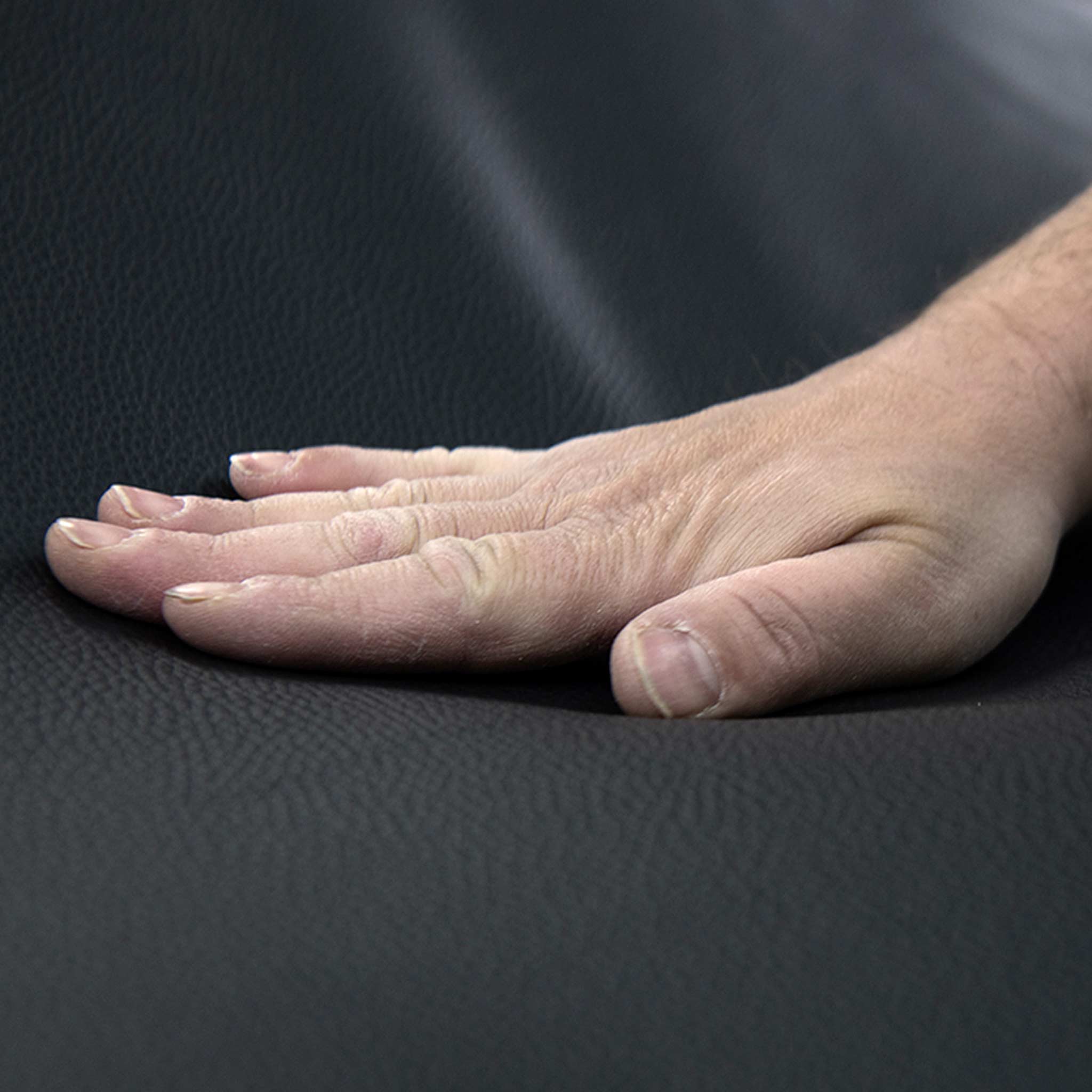Eine Hand berührt nachhaltiges, schwarzes Leder von Frank Sitzmöbel FSM.