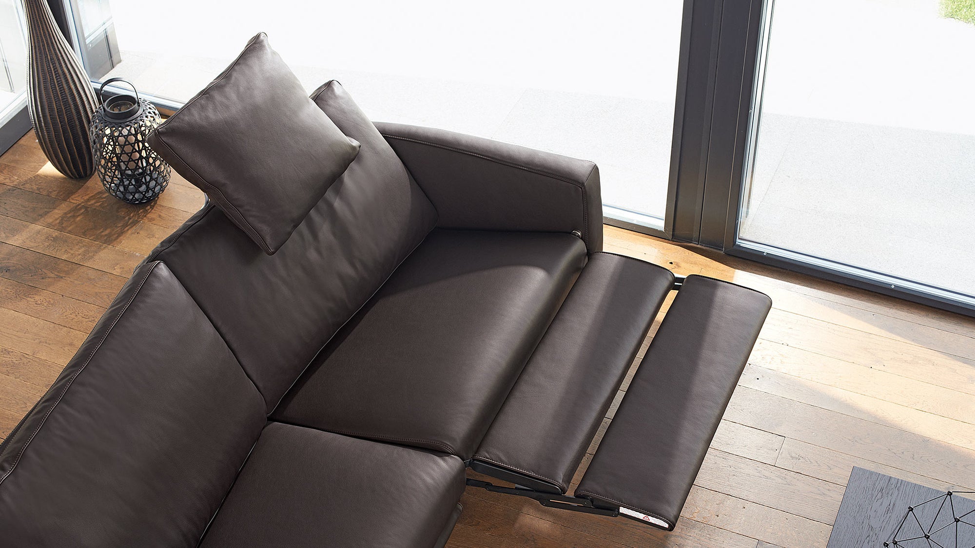 Ein braunes Ledersofa mit Relaxfunktion von Frank Sitzmöbel FSM steht im Wohnzimmer.