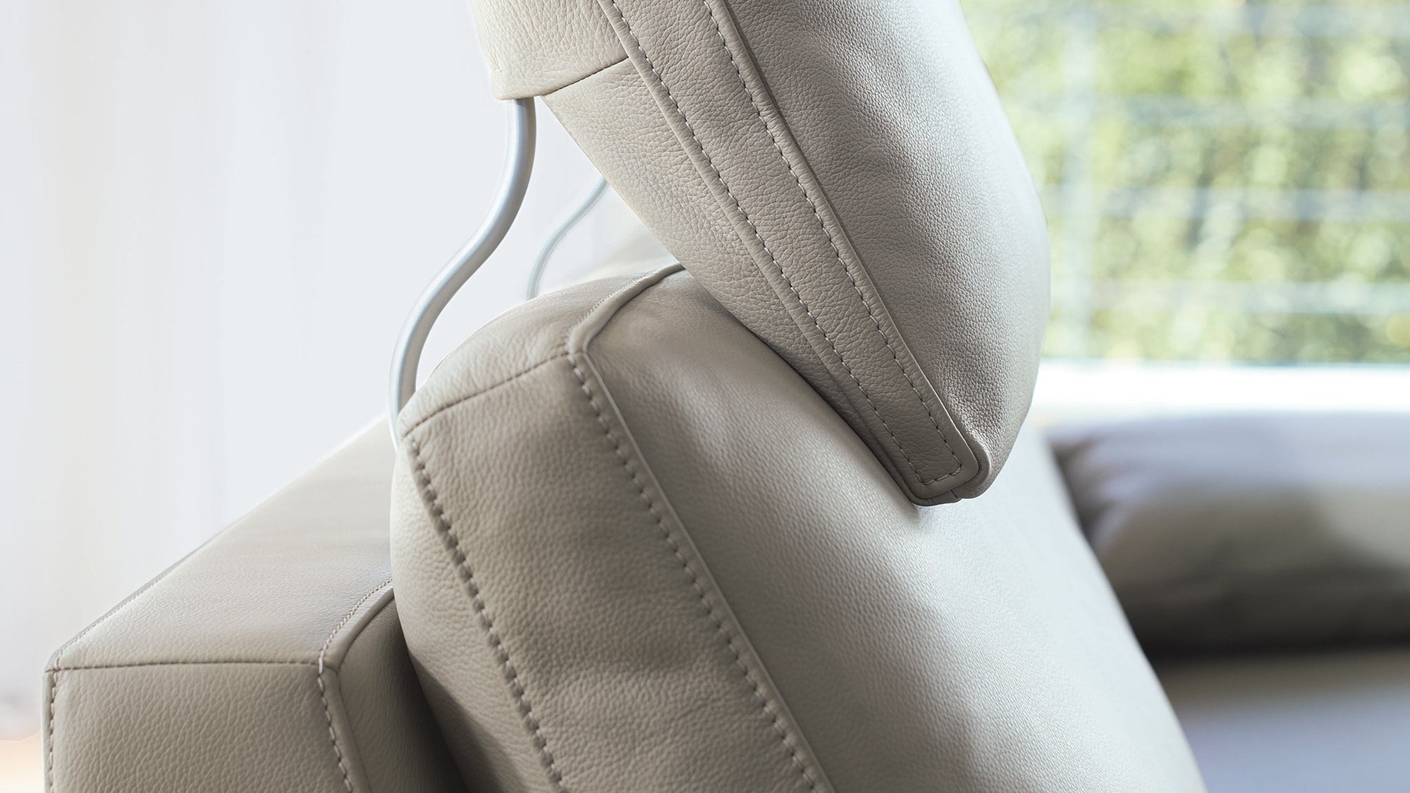 Das beige Ledersofa von Frank Sitzmobel Fsm hat eine verstellbare Kopfstütze.